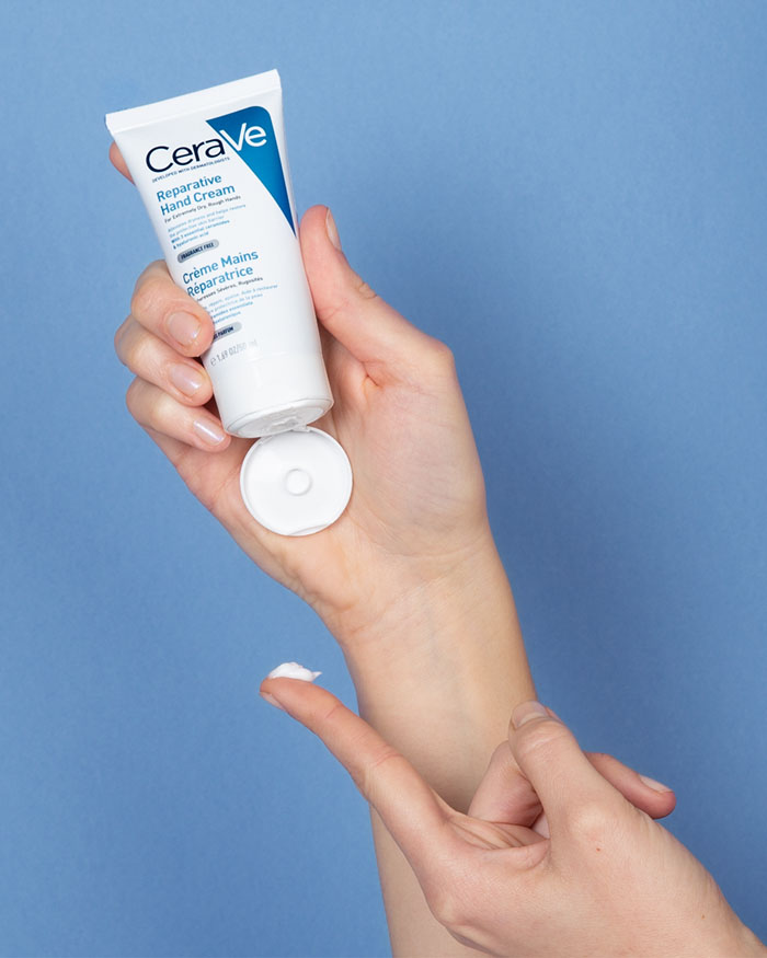 CeraVe hand cream being applied to a hand against a blue background.