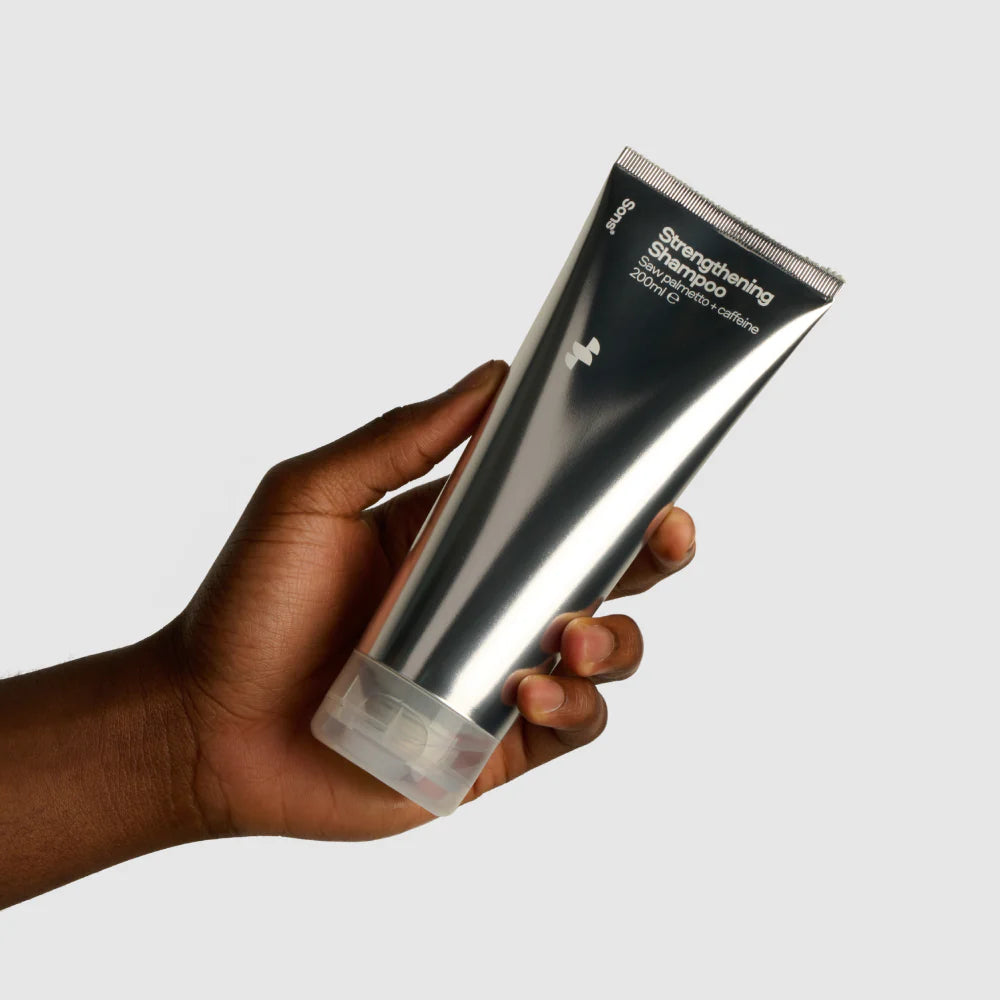 Hand holding a silver shampoo bottle with text on a light gray background