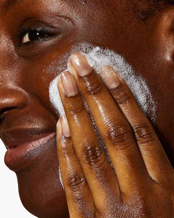Person applying a white cream or foam to their face with a hand