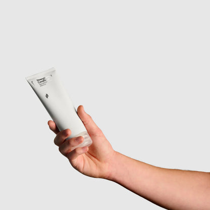 Hand holding a white tube of cream against a light gray background