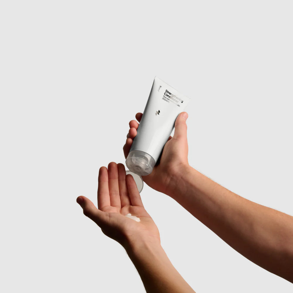 Hand holding a white bottle applying cream to another hand against a light gray background