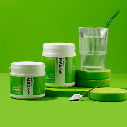 MAG365 magnesium supplement containers with a glass of water on a green background