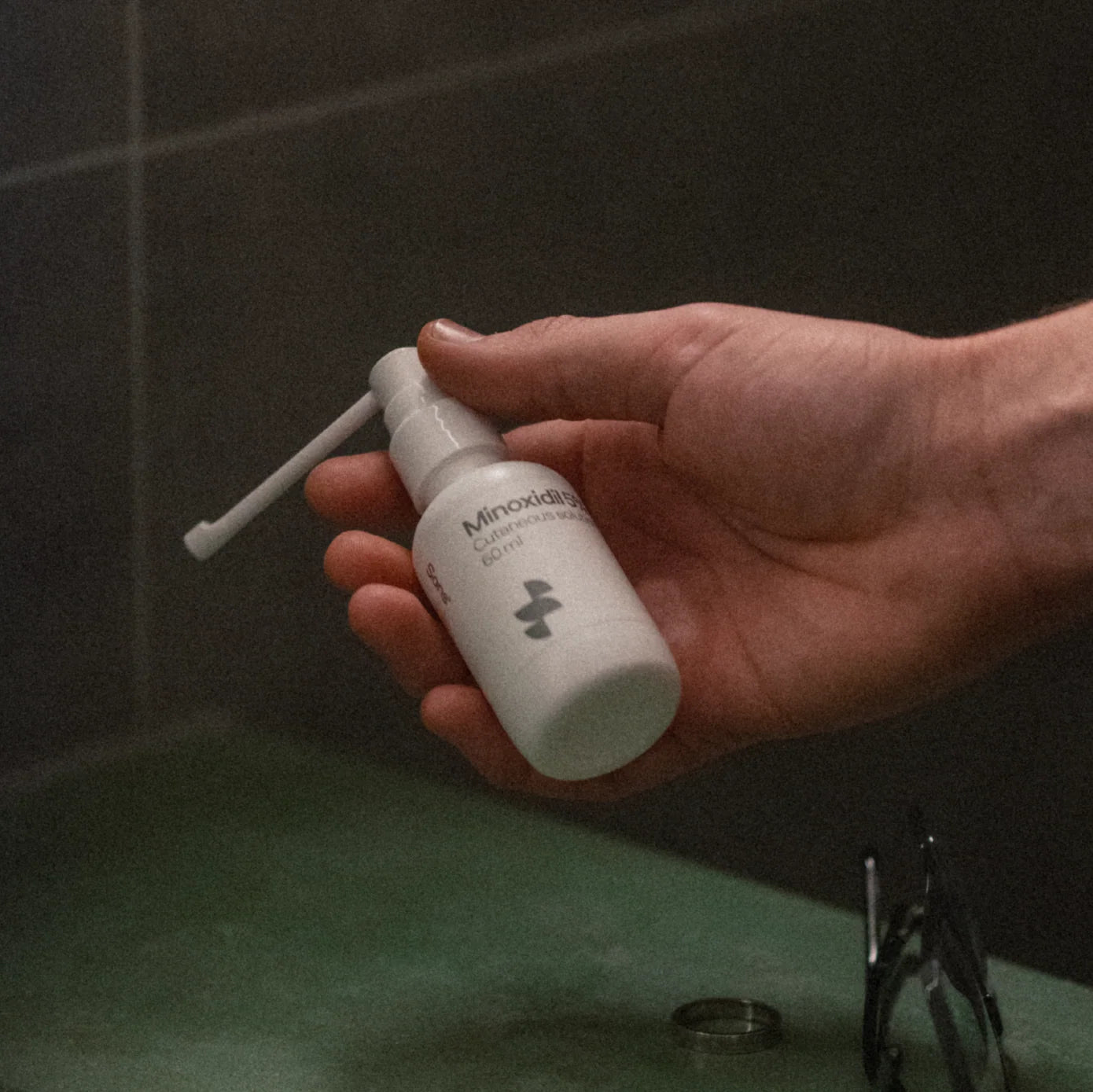 Hand holding a white bottle labeled 'Minoxidil' with a black background