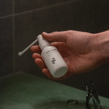 Hand holding a white bottle labeled 'Minoxidil' with a black background
