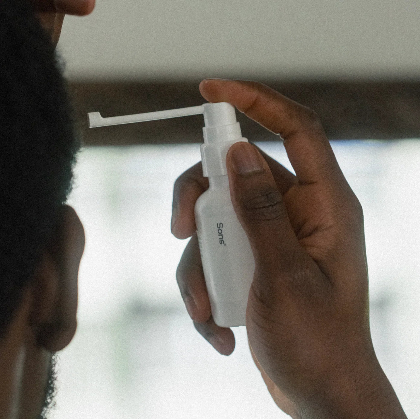 Person using a white spray bottle labeled Sons to their scalp.