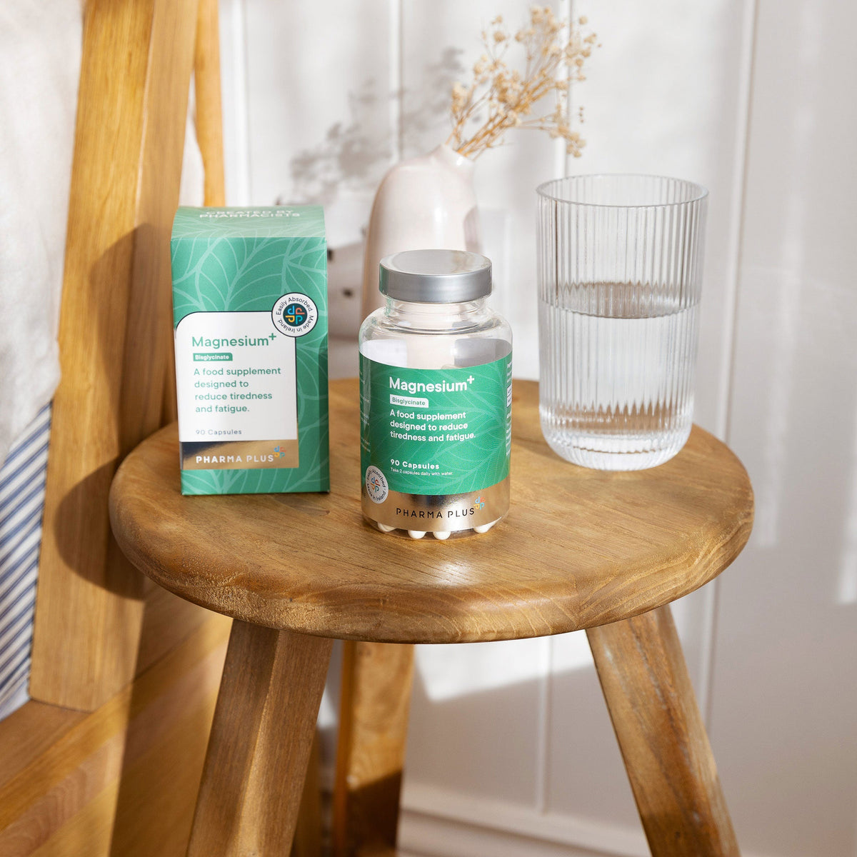 Pharma Plus magnesium supplement bottle and packaging on a wooden stool with a glass of water.