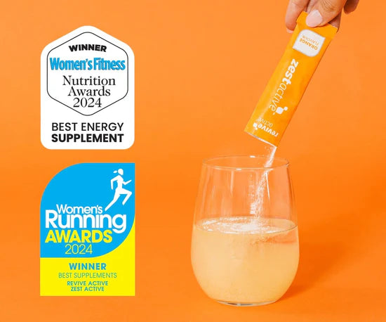 Hand pouring a supplement into a glass with awards for Women's Fitness and Women's Running on an orange background.