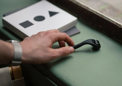 Hand holding a black tool on a green surface with geometric shapes in the background