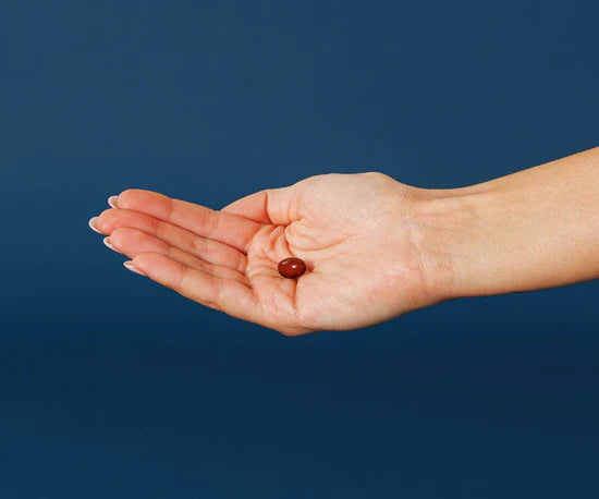 Hand holding a red capsule in middle of palm against a blue background