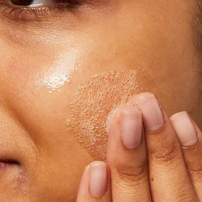 Image of cleanser being lathered on left cheek of someones face.