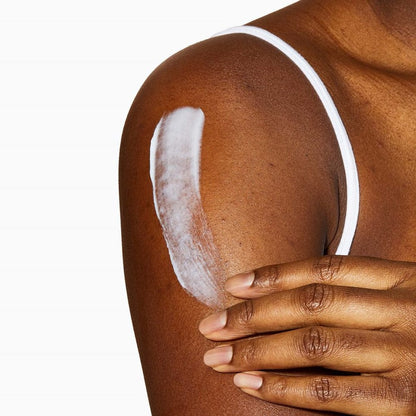 Photograph of lotion or cream being applied to the upper arm. The skin in brown in colour and the lotion is white.